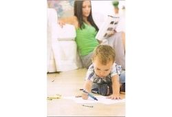 C1 Advanced Speaking Part 2 - A young child drawing on a piece of paper on the floor with a woman in a green top in the background leaning against a white sofa.
