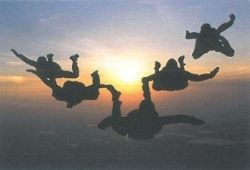 C1 Advanced Speaking Part 2 - Silhouettes of 5 skydivers against a sunset