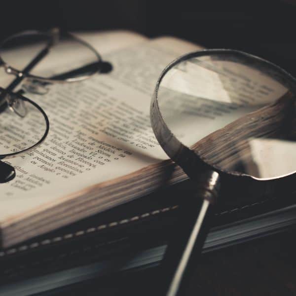 A black and white photo of a magnifying glass and spectacles leaning against a book
