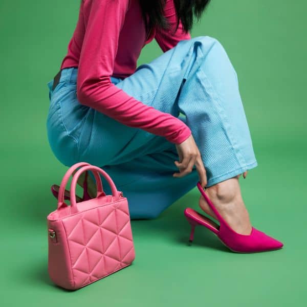 Woman in blue jeans and a red shirt adjusting her red high heels with her pink handbag beside her against a green background - Paraphrasing C1 Advanced Writing part 1 Questions