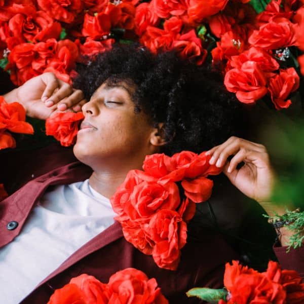 Dark haired person in a jacket and white T shirt sleeping in among several roses - B2 First Speaking Parts 3 & 4: Proven Skills Practice!