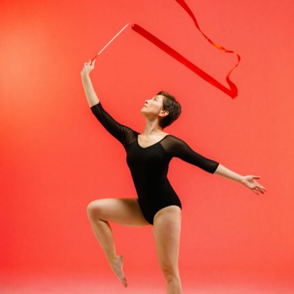 A short haired woman in a black leotard dancing with a prop against a red background - Paraphrasing IELTS Writing Task 2 Questions