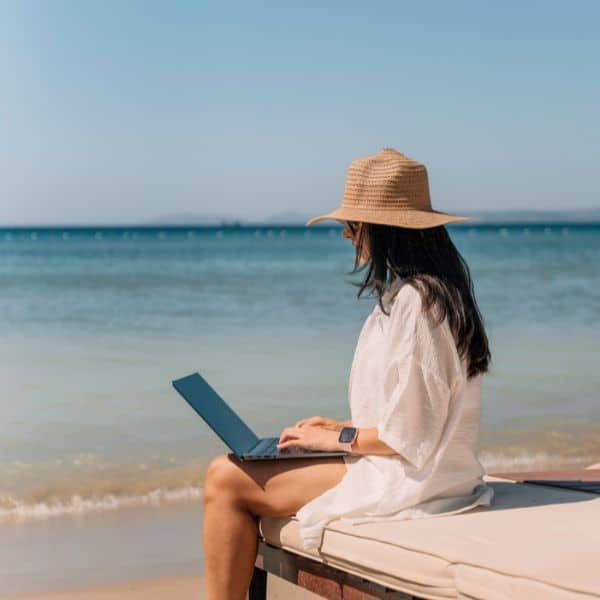 seated woman wearing a sunhat at a beach with a laptop on her knee - Cambridge C1 Advanced Writing Questions