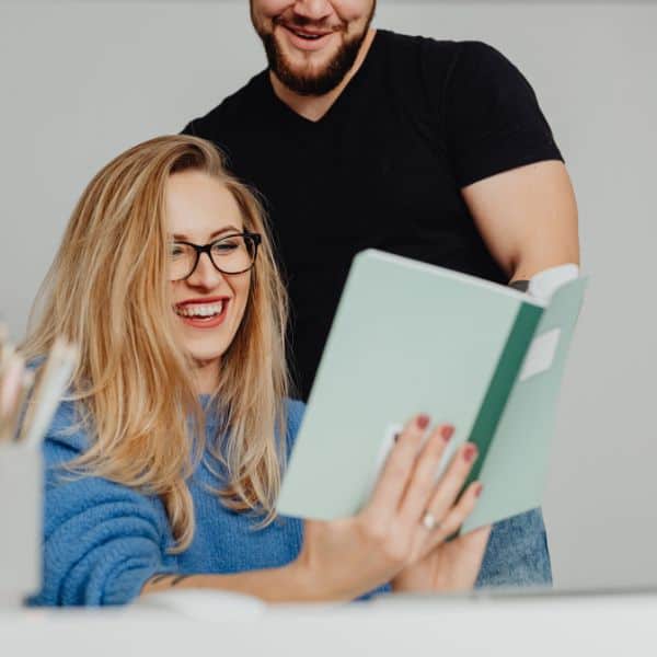 Smiling standing man and seated woman looking at a notebook woman - How to Write a C1 Advanced Report: A Step-by-Step Guide