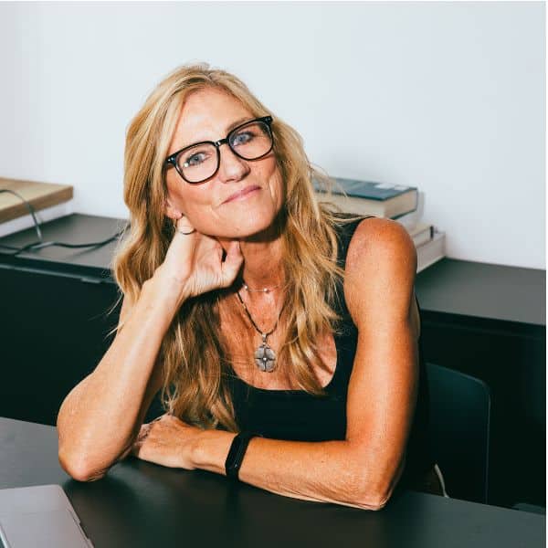 A smirking blonde woman in a black sleeveless dress sitting with her elbow on a black desk, leaning her head on one hand - Better C1 Advanced Speaking Part 2: Answer Structure